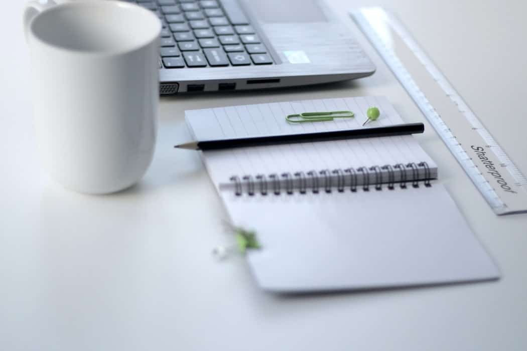 A white notebook laying open next to a white mug and laptop