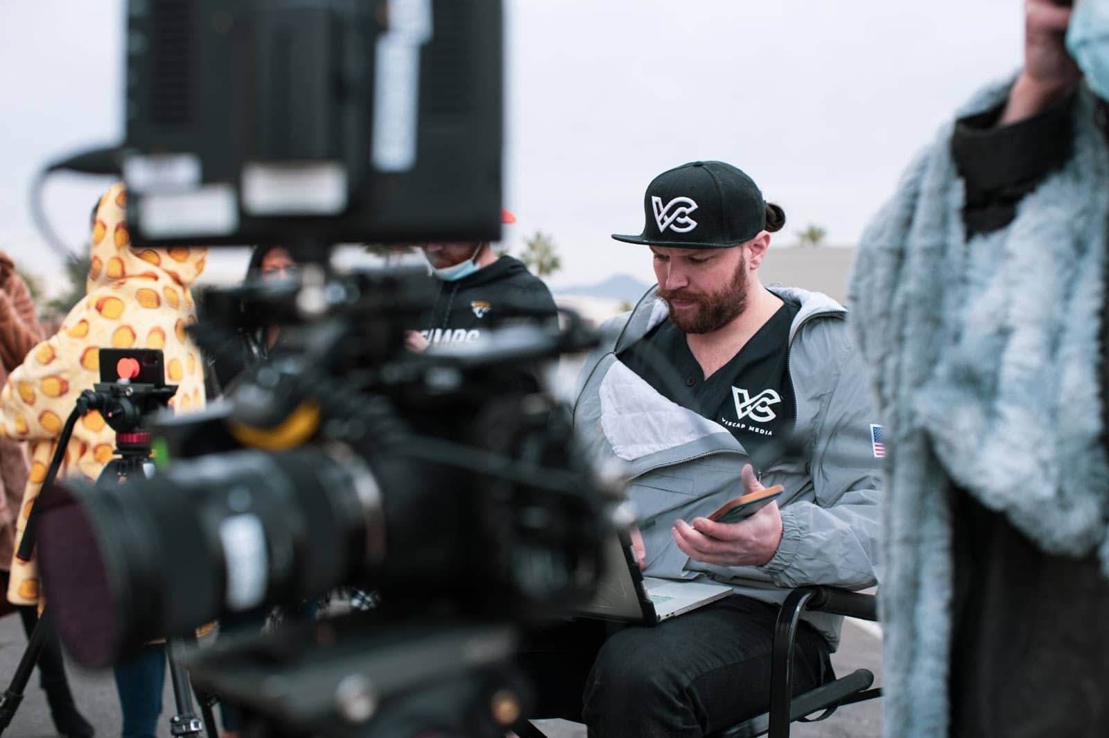 Man sitting in directors chair behind a camera reading notes from a notebook.