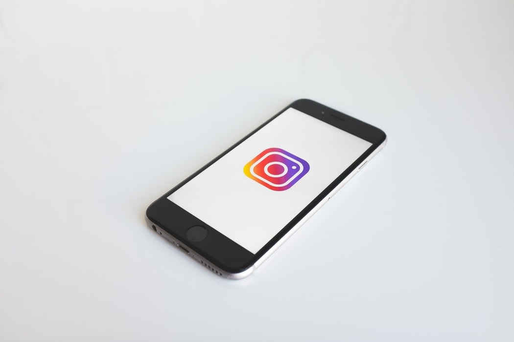 A cellphone showing the instagram logo laying on a white surface.